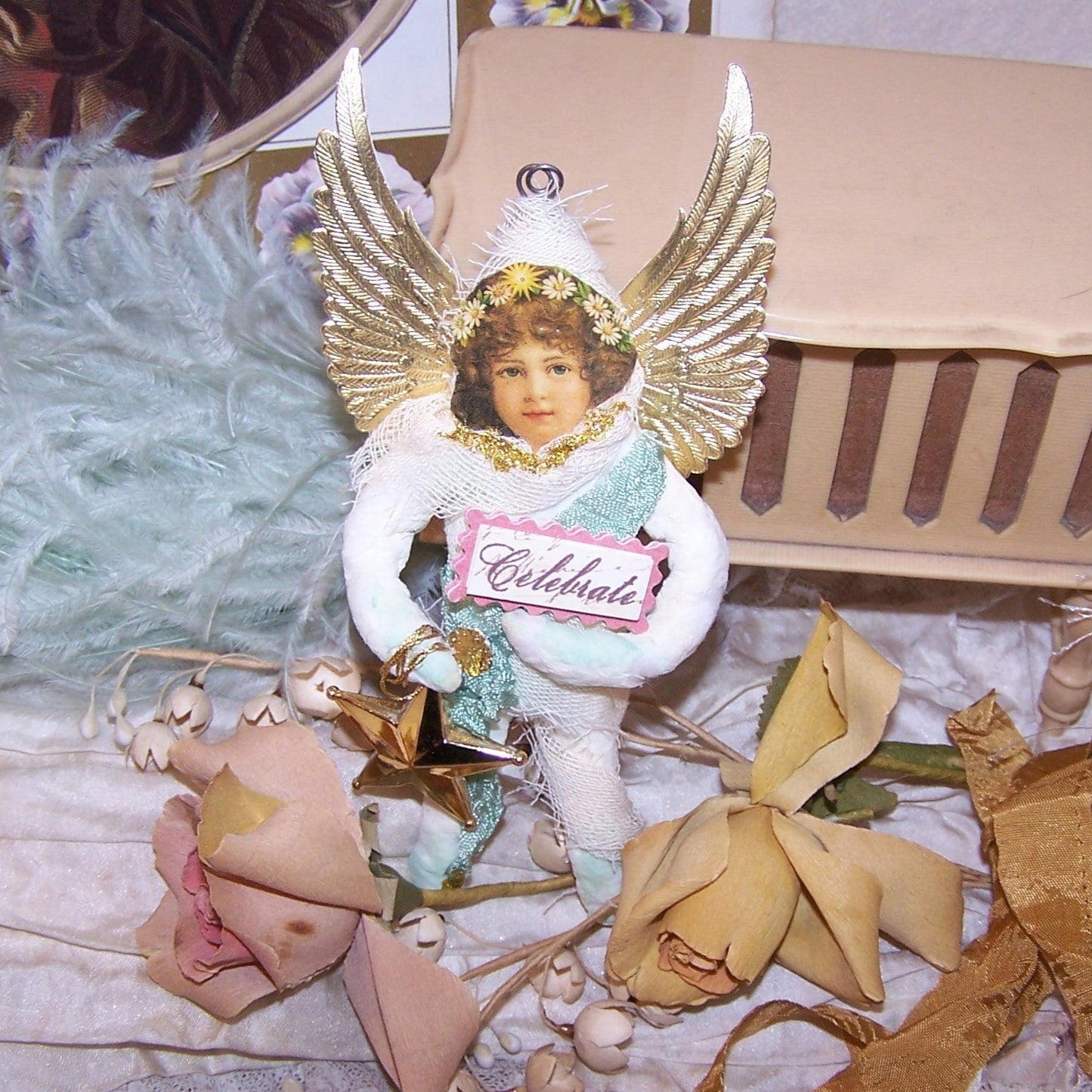 In a Victorian Revival style, a Spun Cotton Guardian Angel wearing an aqua colored rayon sash and carrying a star as well as a small sign reading CELEBRATE.