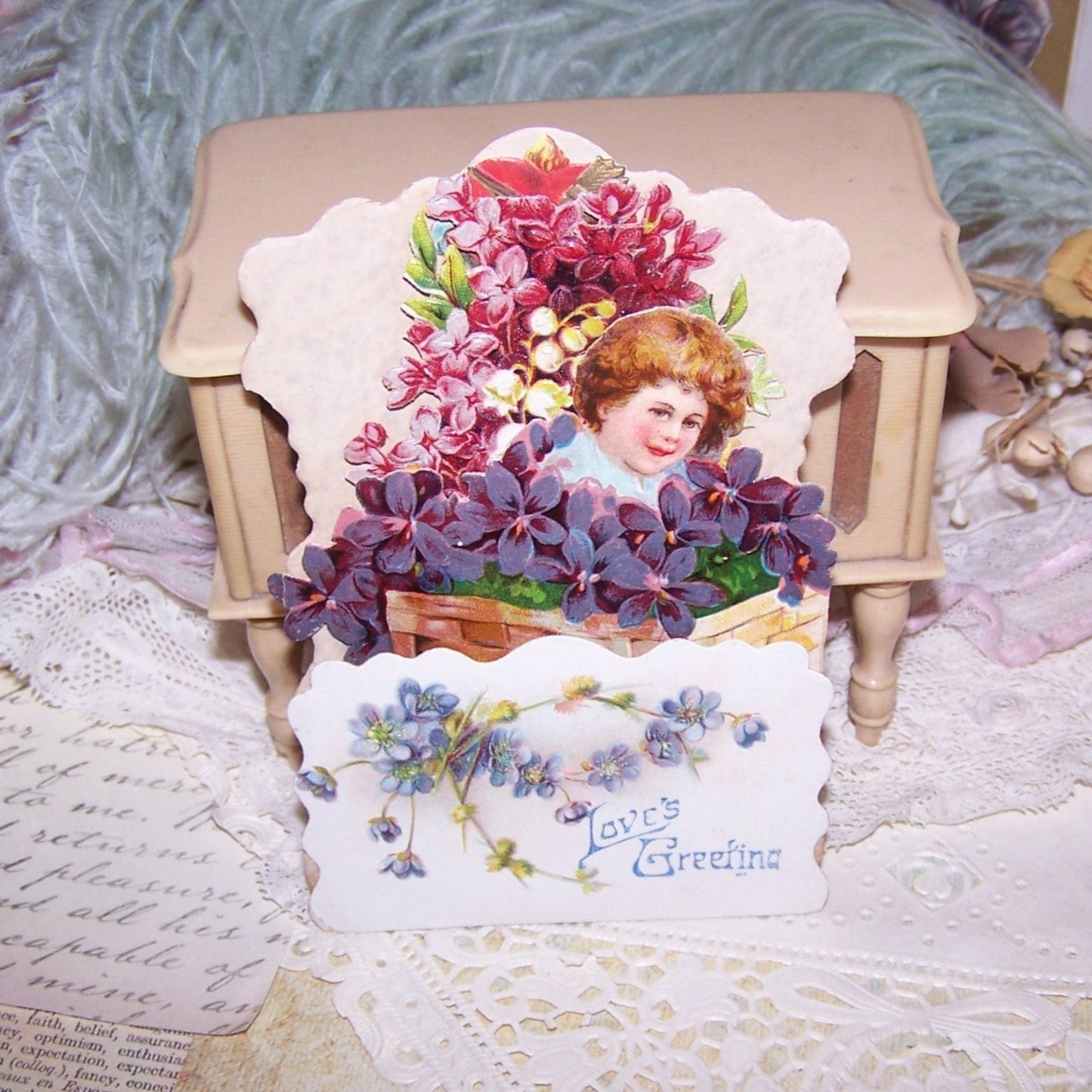Antique German fold down/pull down Valentines Day card featuring a girl in a basket of violets. Sentiment is LOVE'S GREETING. Used but nice condition.