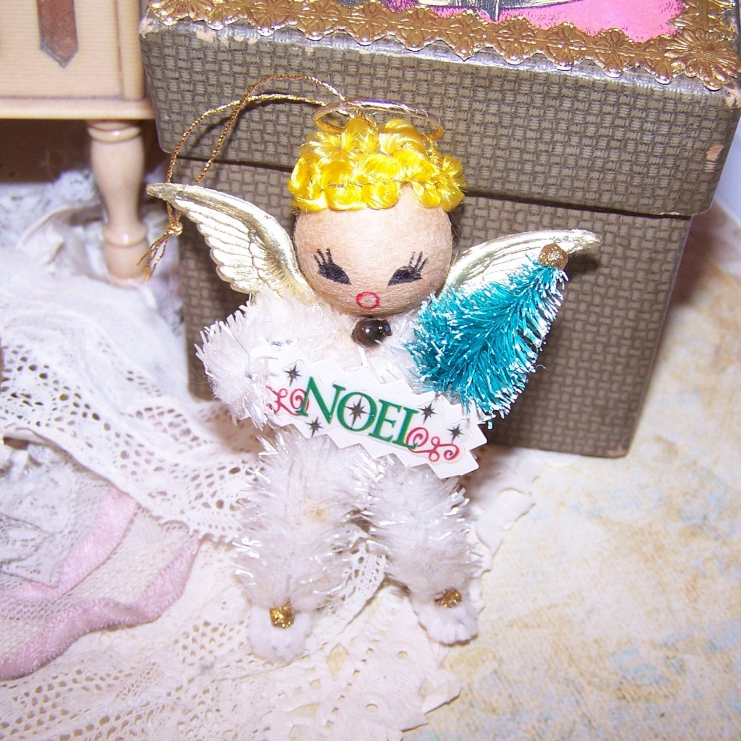 Decorative angel ornament with 'NOEL' on a lace surface