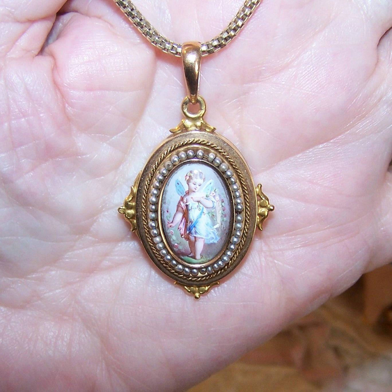 Antique Victorian 14K Gold locket pendant with handpainted enamel or porcelain fairy to the front. Oval front is surrounded by natural pearls strung on wire.