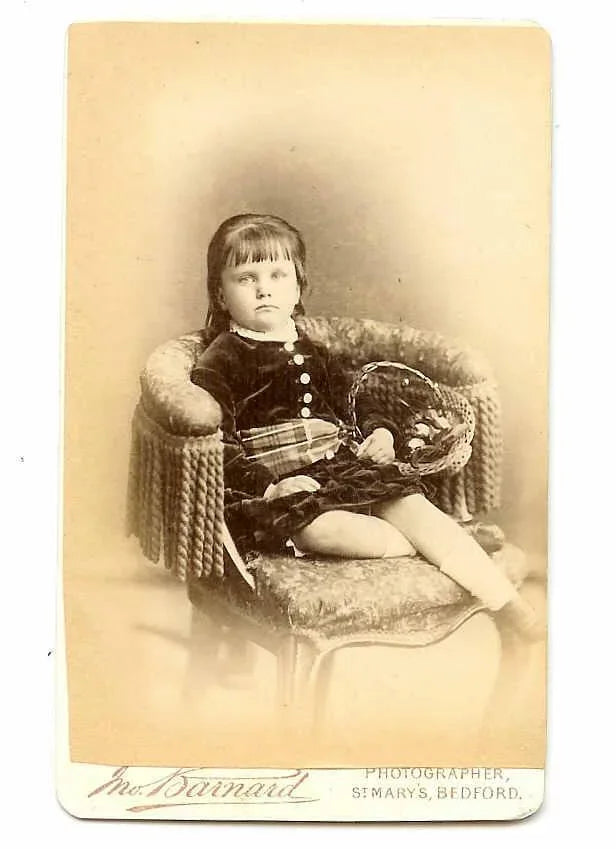 Antique Victorian cabinet card photograph depicting a young girl resting in a chair. The child appears to be dressed in a velvet outfit with tartan sash.