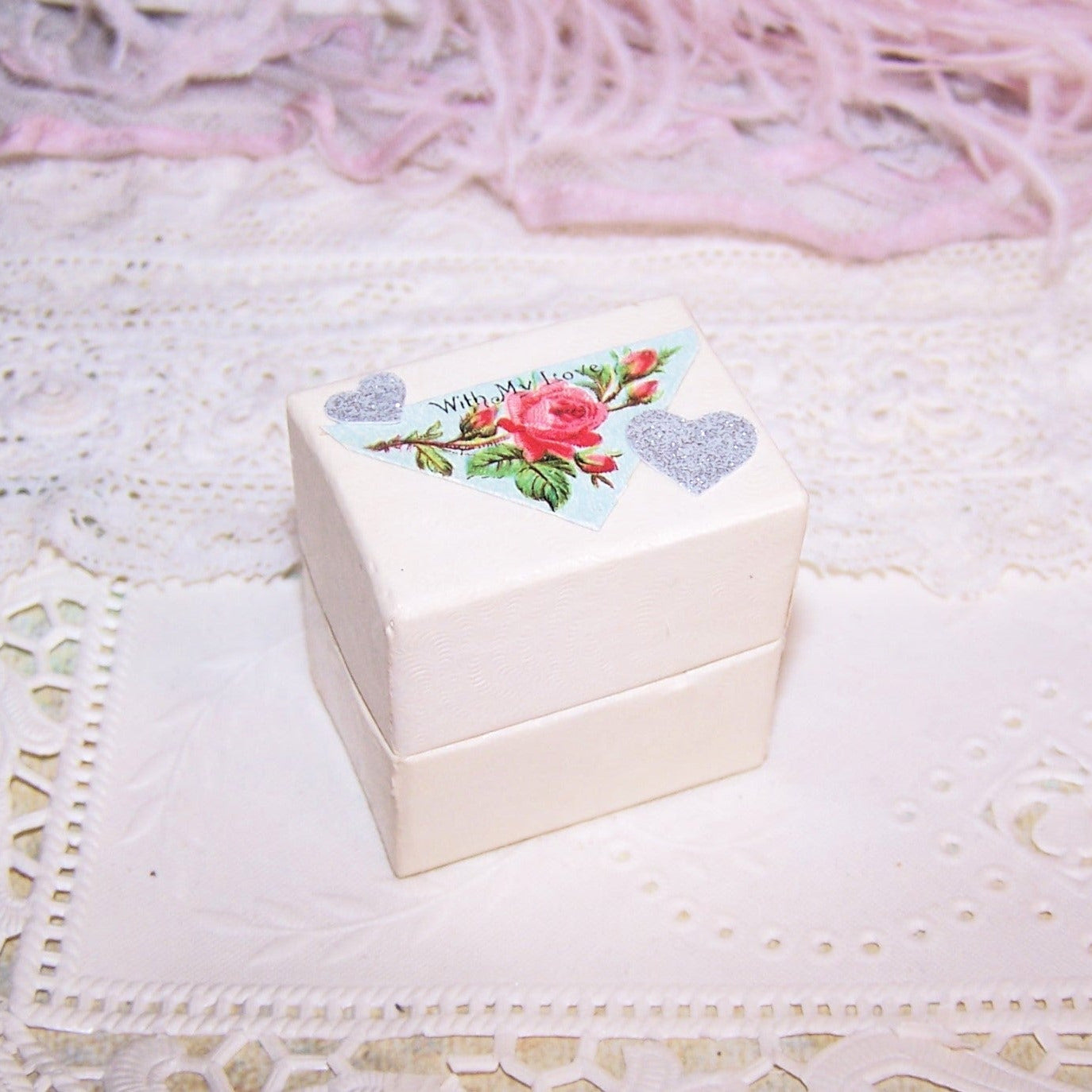 Cream paper ring box with slotted insert on the inside and Antique Victorian die cut reading WITH MY LOVE to the top. 1-1/2" high; base is 1-7/16" x 1-1/16"