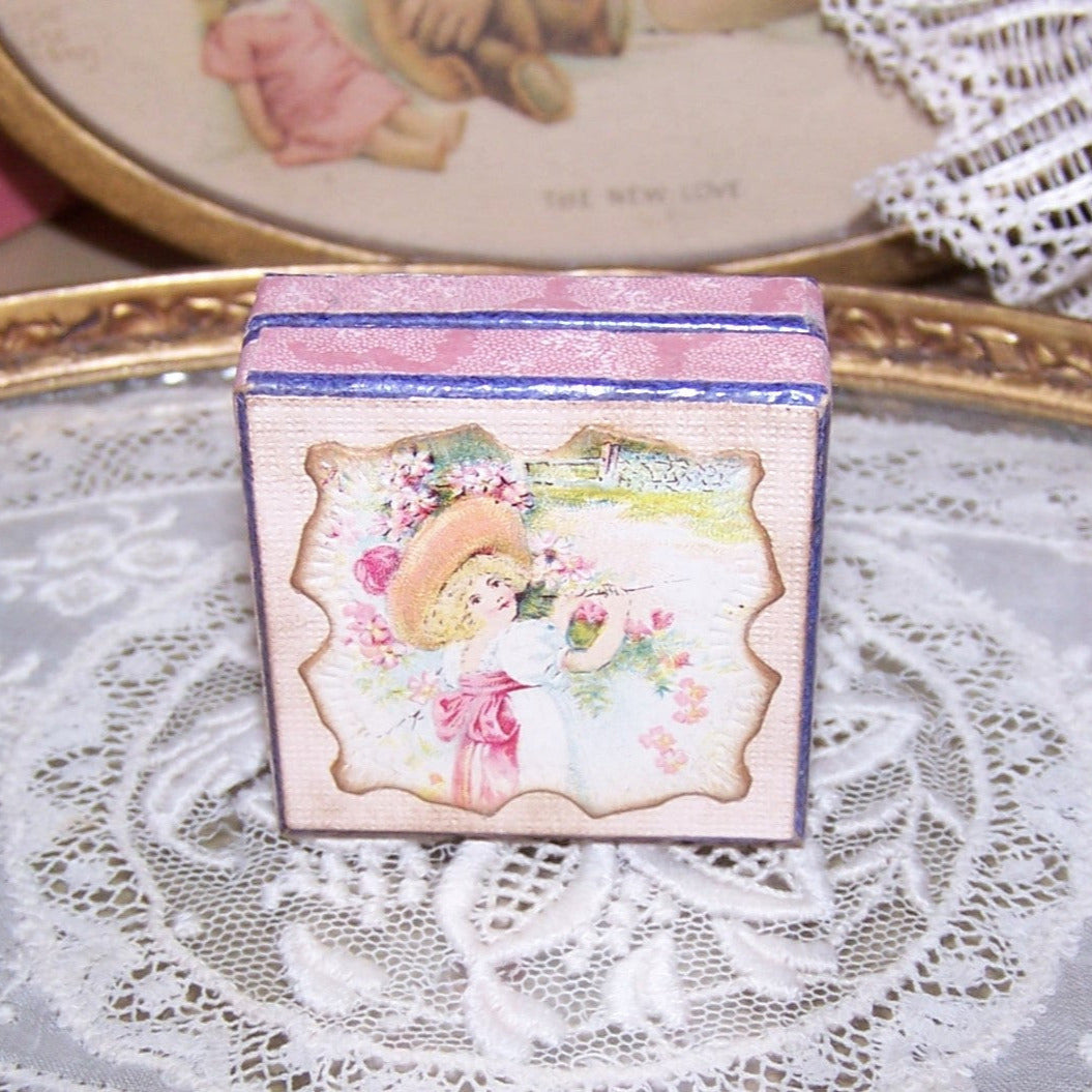 French C.1920 lidded jewelry box with image of a young girl standing against a wall covered in flowers. The box measures 1-5/8" square; depth is 5/8".