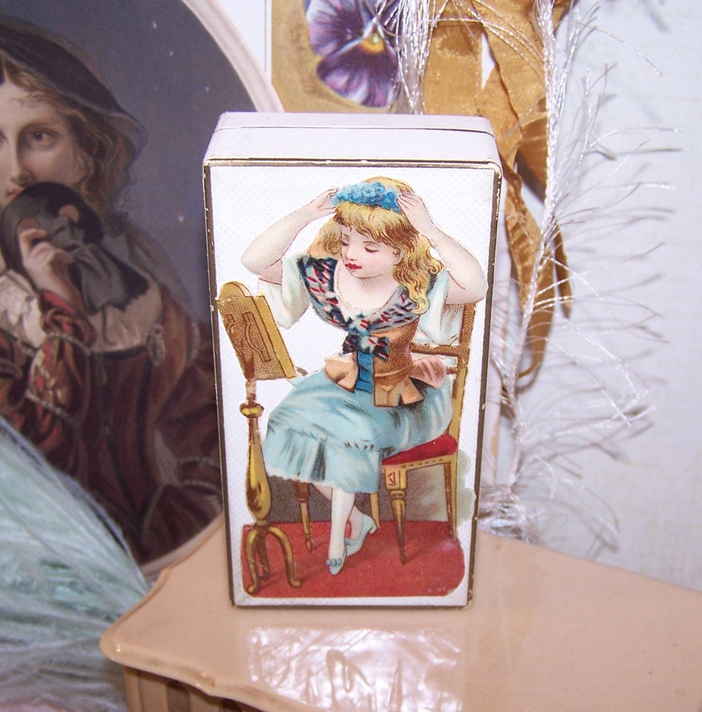 Antique paper jewelry box that might have held a flask of perfume or mini doll! Victorian die cut to top of a young lady, the box is 4" x 2" x 1-1/16" deep.