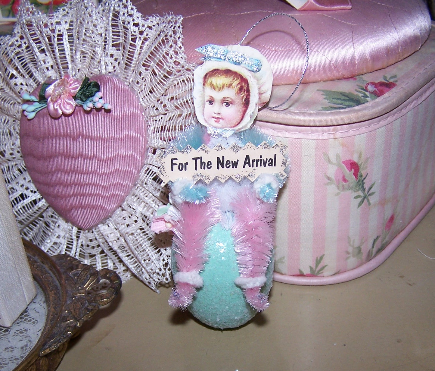 Handmade OOAK Victorian Revival chenille ornament. A Baby Girl sits on a sparkly Aqua Egg and holds a sign that reads FOR THE NEW ARRIVAL. Christening Gift Idea