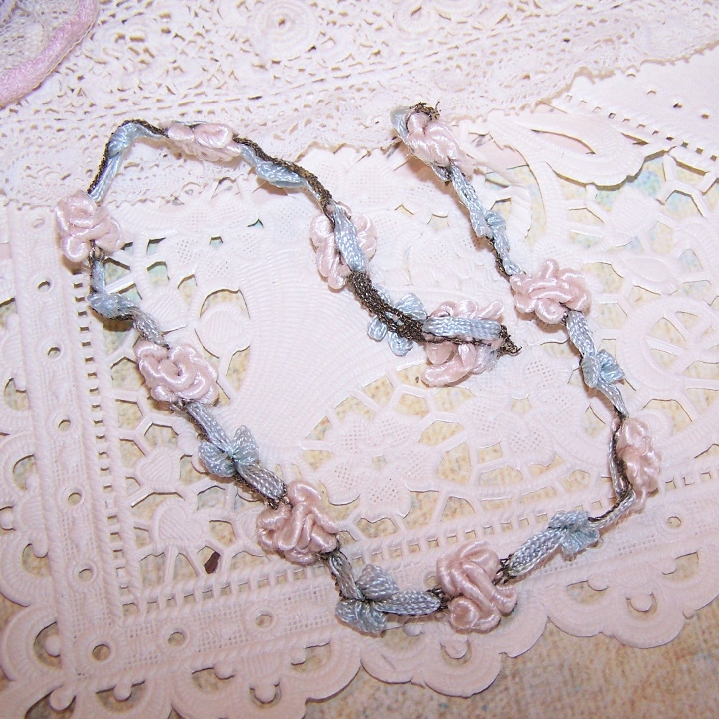 From France, may I offer this short 10" piece of Art Deco rococo garland trim. To the touch, the trim is silky soft and smooth and is composed of loopy pinky cream buds with pale blue rayon trim (stitched with gold thread) sides. Width at each "bud" is 3/8". Very, very clean with no stains or smell.