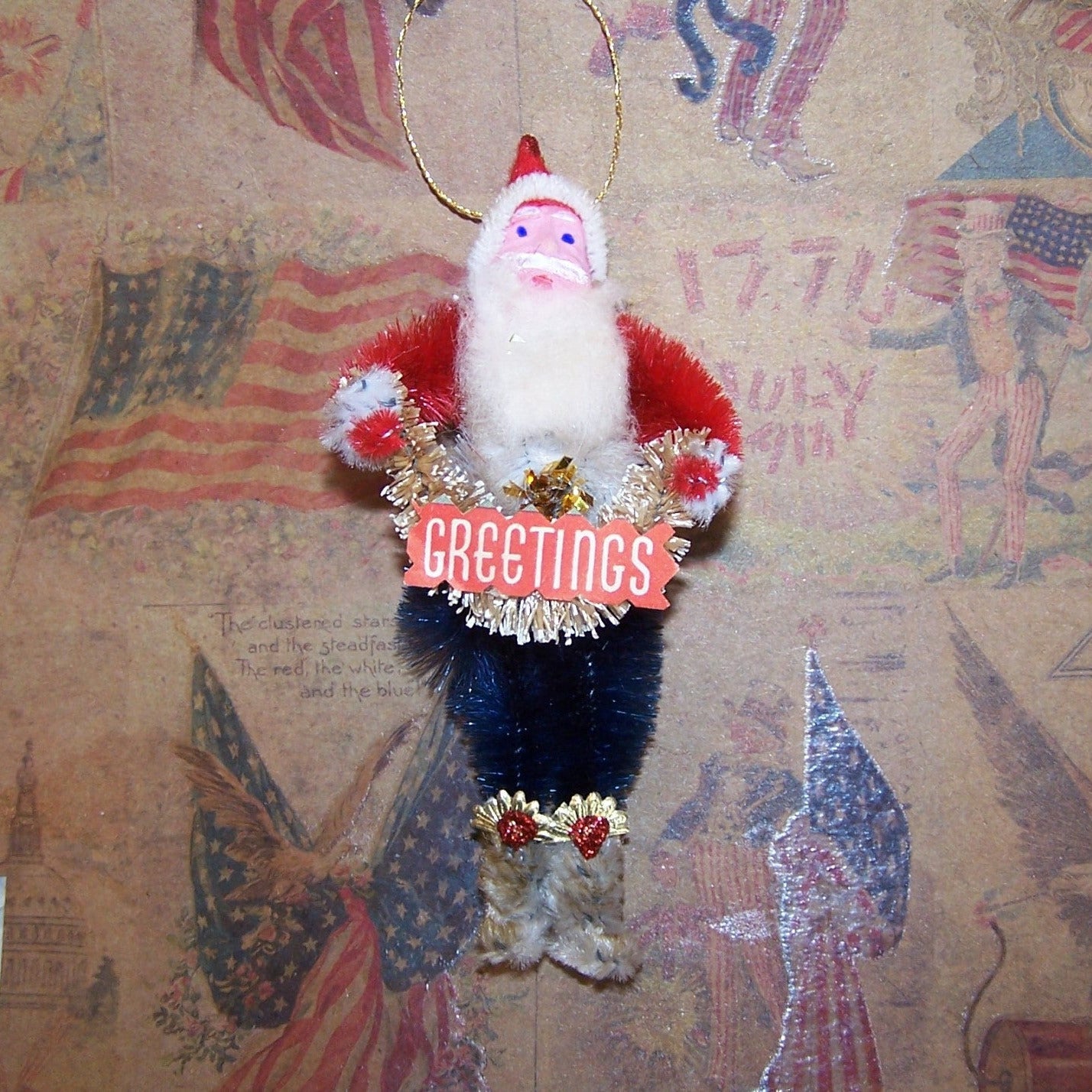 Red, White & Blue chenille Christmas ornament of Santa Claus. Retro inspired, Santa is very patriotic & carries a bottle brush garland; sentiment is GREETINGS!