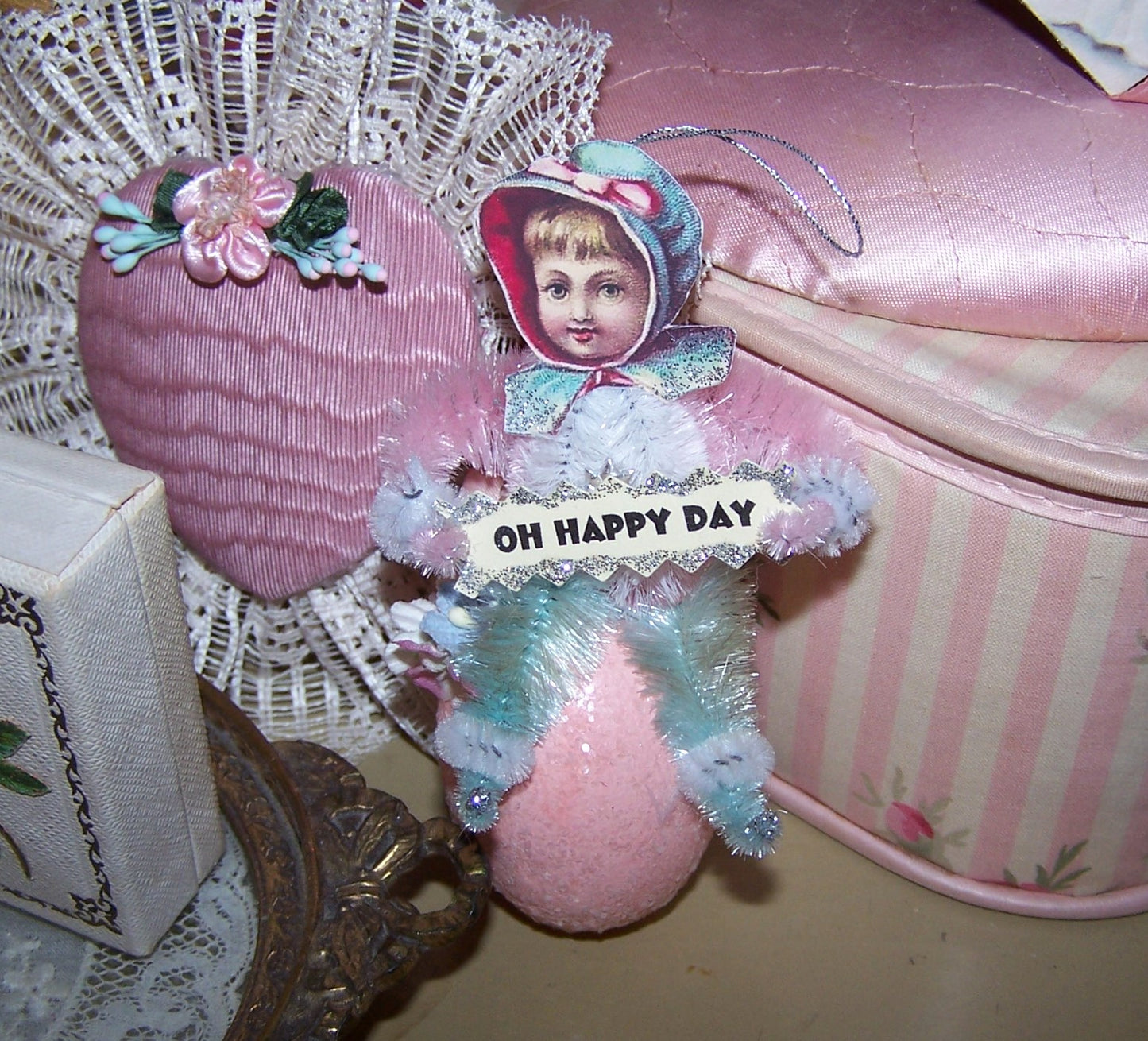 Handmade Victorian Revival Spring chenille ornament. A baby girl sits on a sparkly Pink Egg and holds a sign that reads OH HAPPY DAY. All occasion gift idea!