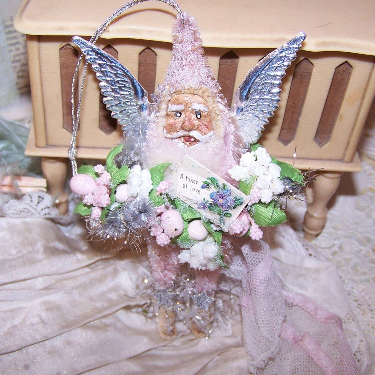 Santa in pink chenille with silver dresden paper wings. Santa carries a garland of flowers and berries and has a handpainted clay face similar to those of vintage japan holiday ornaments. stands about 4 inches high. one of a kind.