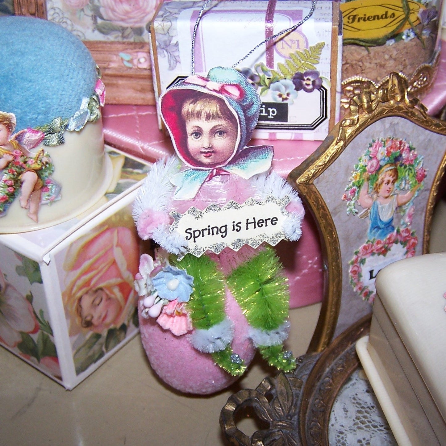Handmade Victorian Revival chenille ornament. A little girl sits on a sparkly Pink Egg and holds a sign that reads SPRING IS HERE! All occasion gift decoration.