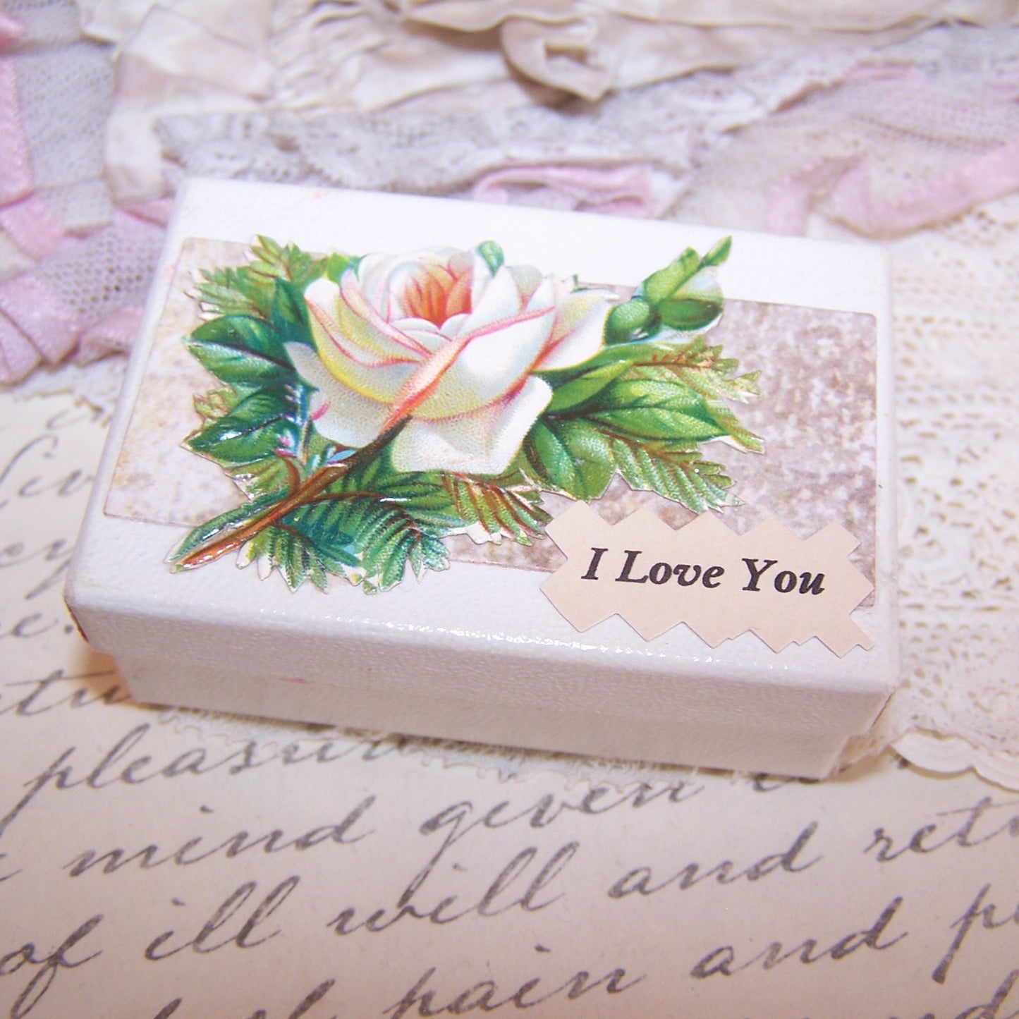 Upcycled paper box for a small item. Lid displays an Antique Victorian die cut of a white rose. Sentiment is I LOVE YOU. 2-1/2" x 1-3/4"; depth is 15/16".