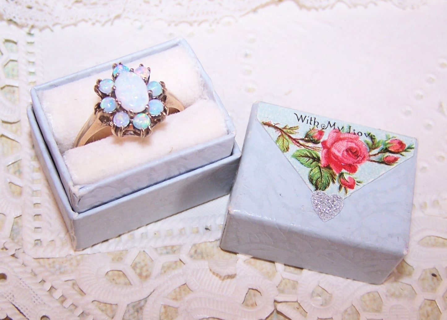 Light blue paper ring box with slotted insert on the inside and Antique Victorian die cut reading WITH MY LOVE to the top. 1-1/4" x 15/16" x 1-3/16" high.