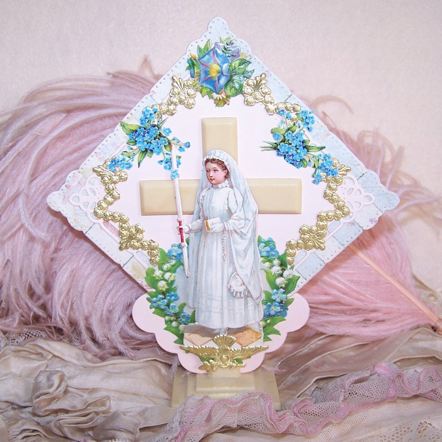 One of a kind handcrafted first communion souvenir. Art deco celluloid cross base with applied Antique Victorian dies cuts including a young girl dressed in First Communion attire. Blue Forget me Nots and gold paper dresden trim complete the design.