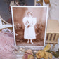 Antique Victorian cabinet card depicting a young girl graduate.  The lady not only wears flowers in her hair and on her dress, but she is surrounded by them. 