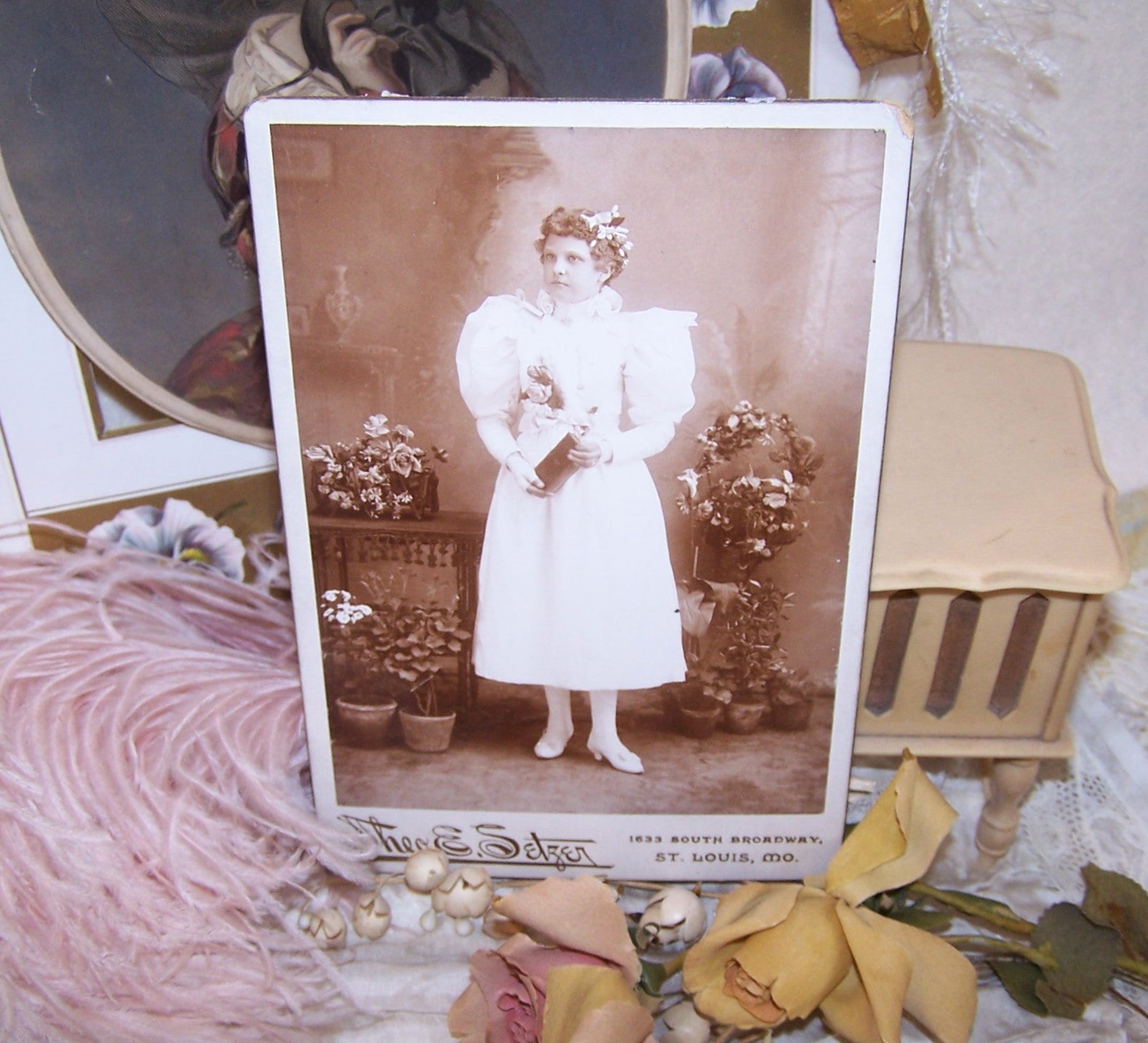 Antique Victorian cabinet card depicting a young girl graduate.  The lady not only wears flowers in her hair and on her dress, but she is surrounded by them. 