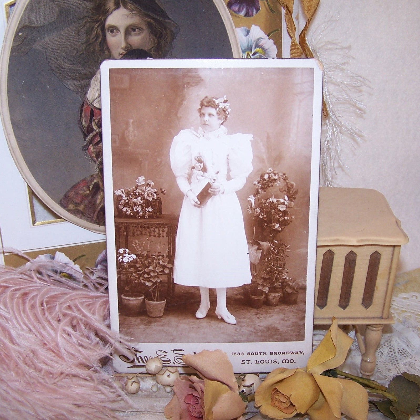 Antique Victorian cabinet card depicting a young girl graduate.  The lady not only wears flowers in her hair and on her dress, but she is surrounded by them. 