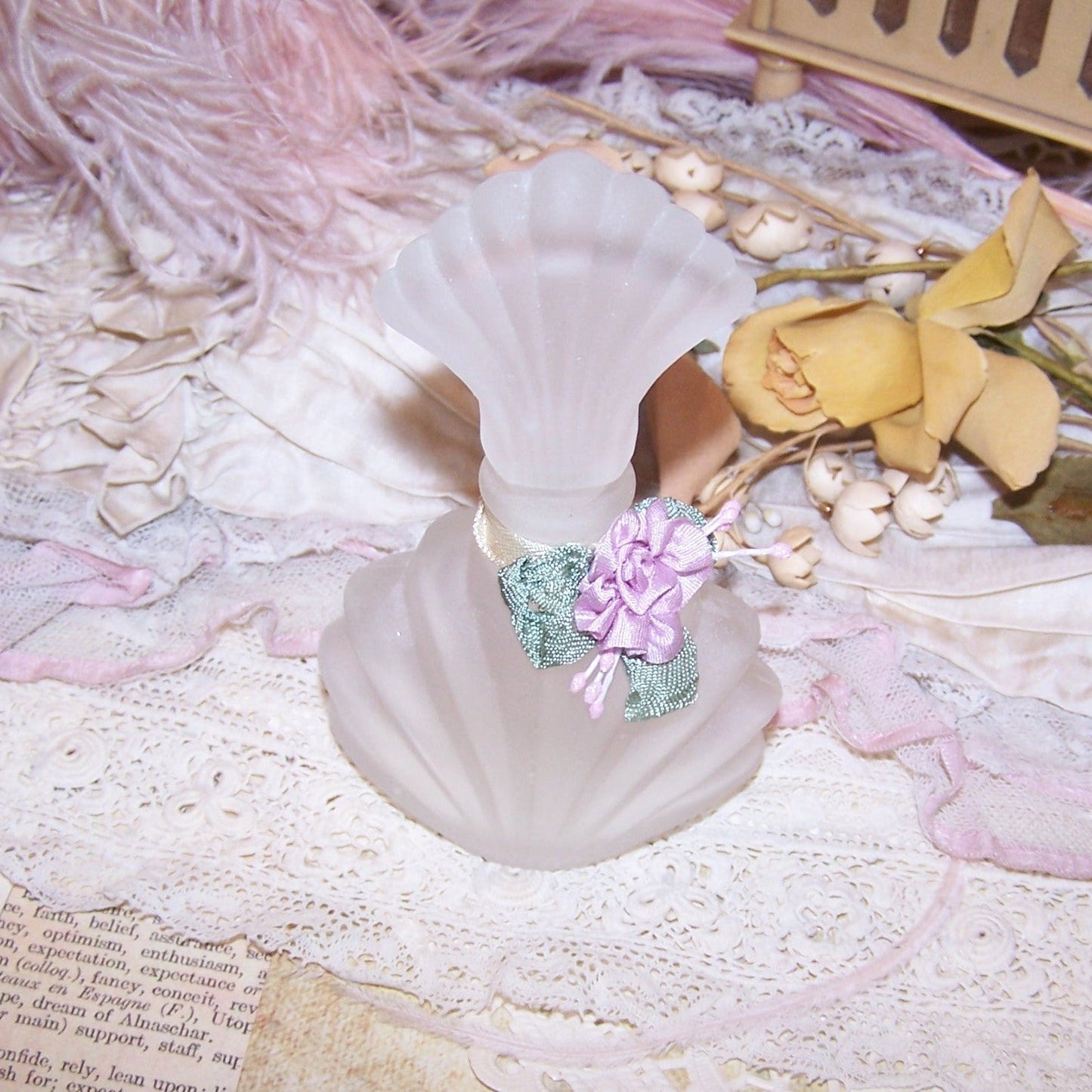 A spruced up frosted glass perfume bottle.  In unused condition, the neck of the piece sports a French Revival ribbonwork applique of lavender silk.  
