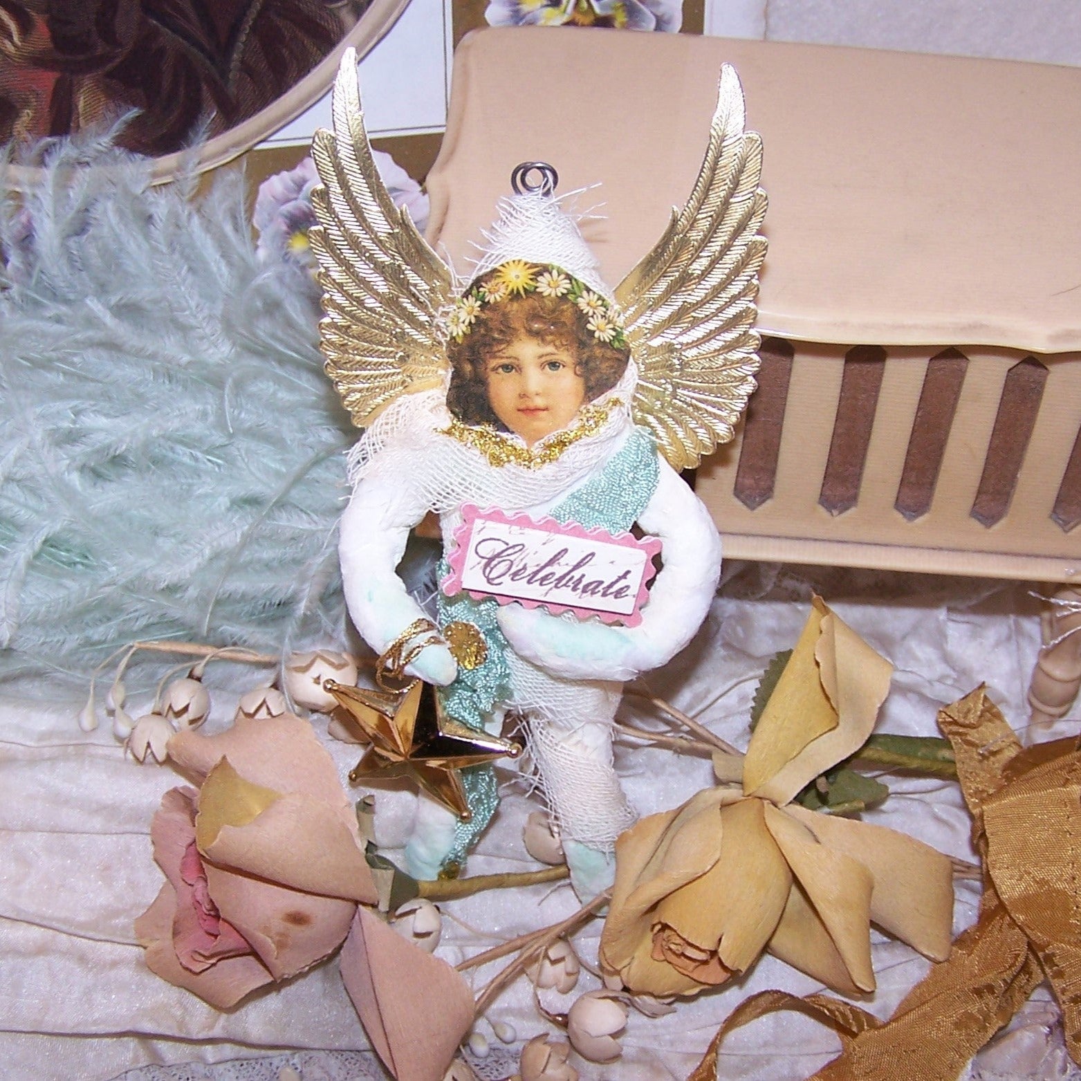 In a Victorian Revival style, a Spun Cotton Guardian Angel wearing an aqua colored rayon sash and carrying a star as well as a small sign reading CELEBRATE.  