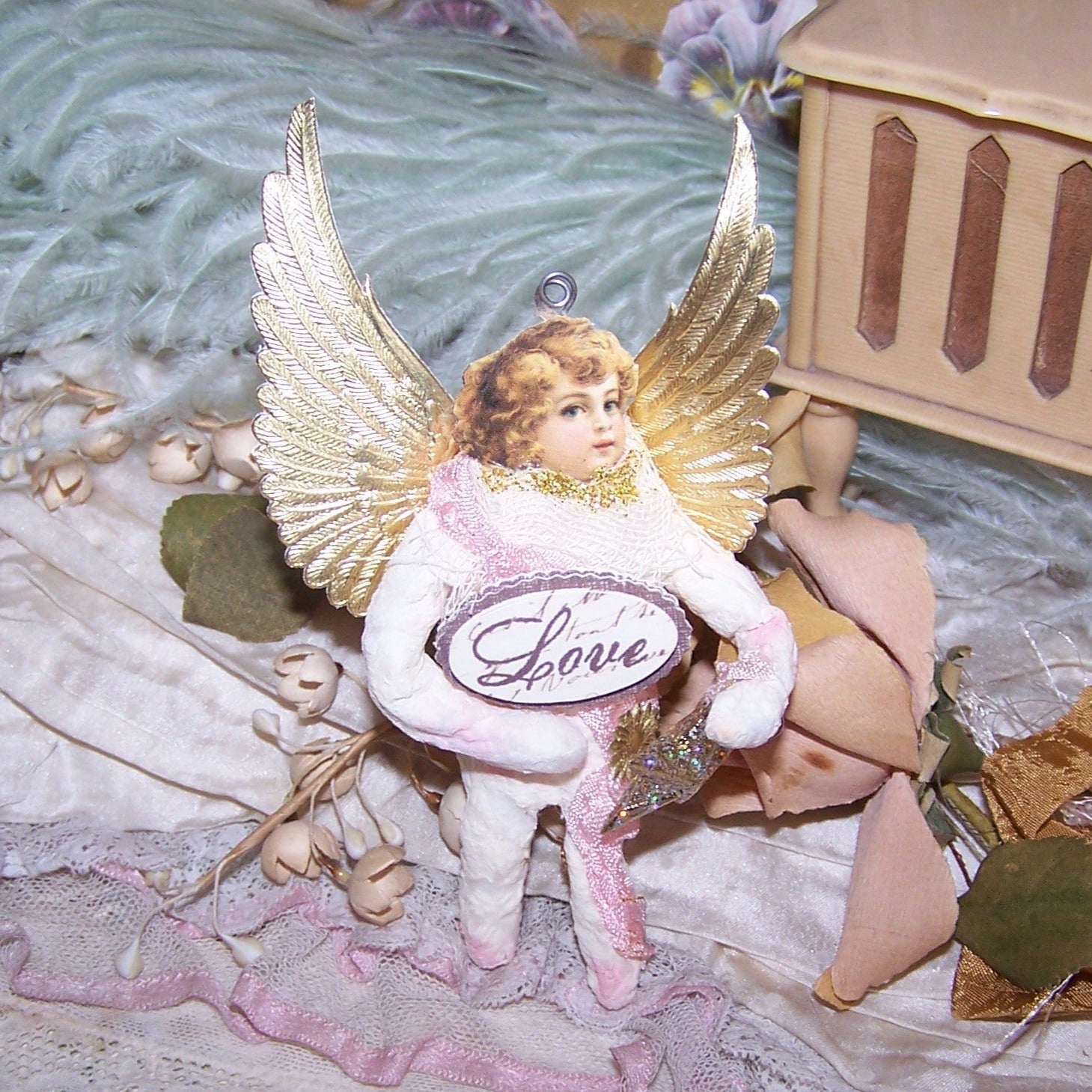 In a Victorian Revival style, a Guardian Angel of Spun Cotton wearing a pink rayon sash and carrying a Star as well as a small sign reading LOVE.  