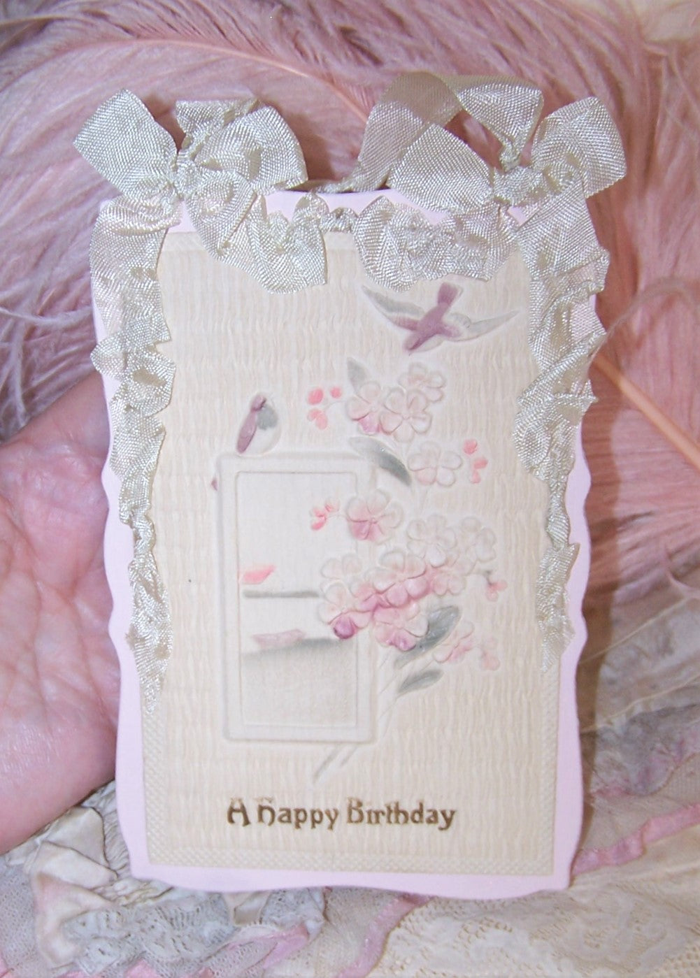 Repurposed flocked postcard  with a design of birds, flowers and pastoral scene; the sentiment to the front is A HAPPY BIRTHDAY. The pastel-colored p/c has been applied to more modern day pink/white cardstock and embellished with some cream rayon ribbon. The reverse of the card is blank but has an additional bit of card as well as a more modern day Victorian image applied - lots of room to write your own personalized sentiment. 