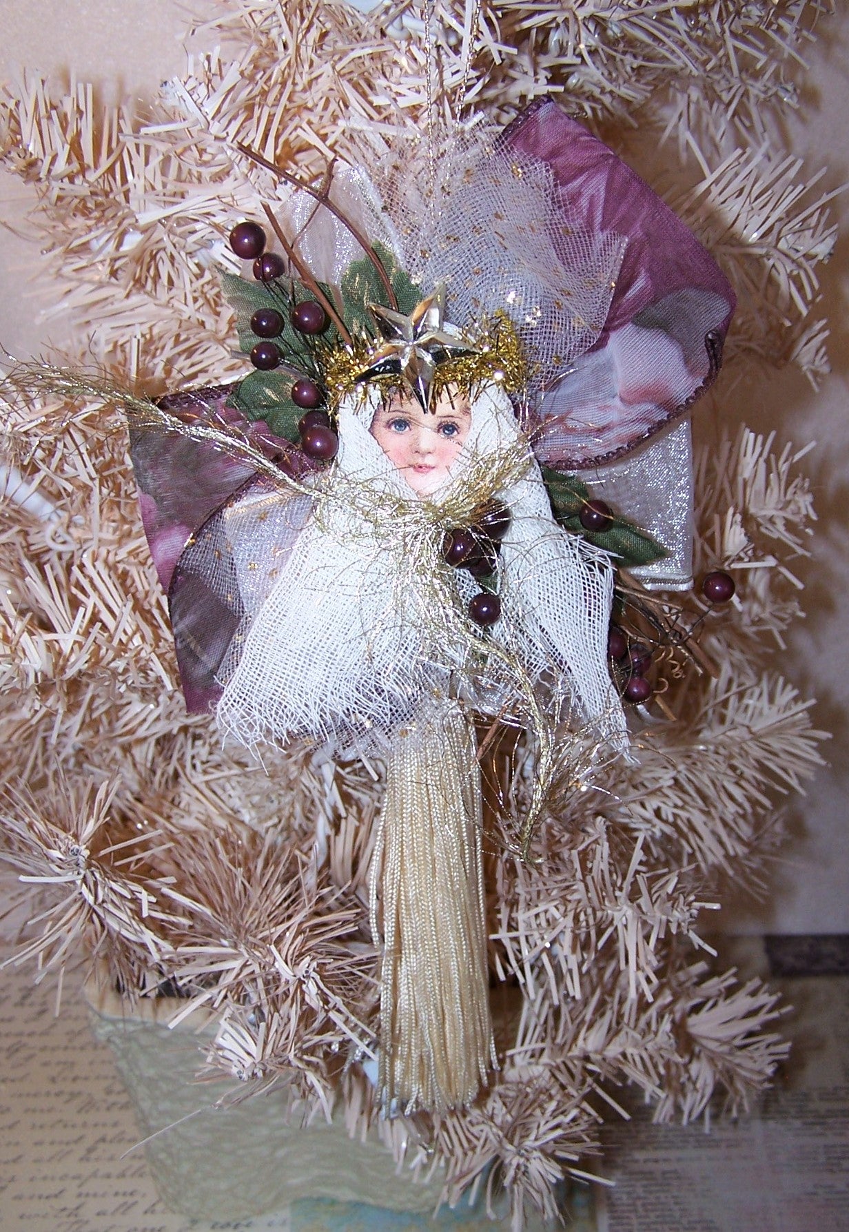 Angel ornament of tulle, gauze, ribbon, twigs and tassel in colors of cream, gold & burgundy. Backed with a wood oval which can be personalized by the new owner