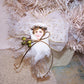An angel ornament made of tulle, gauze, ribbon, cord and a tassel in colors of gold & cream. Backed with a wood heart which can be personalized by the new owner