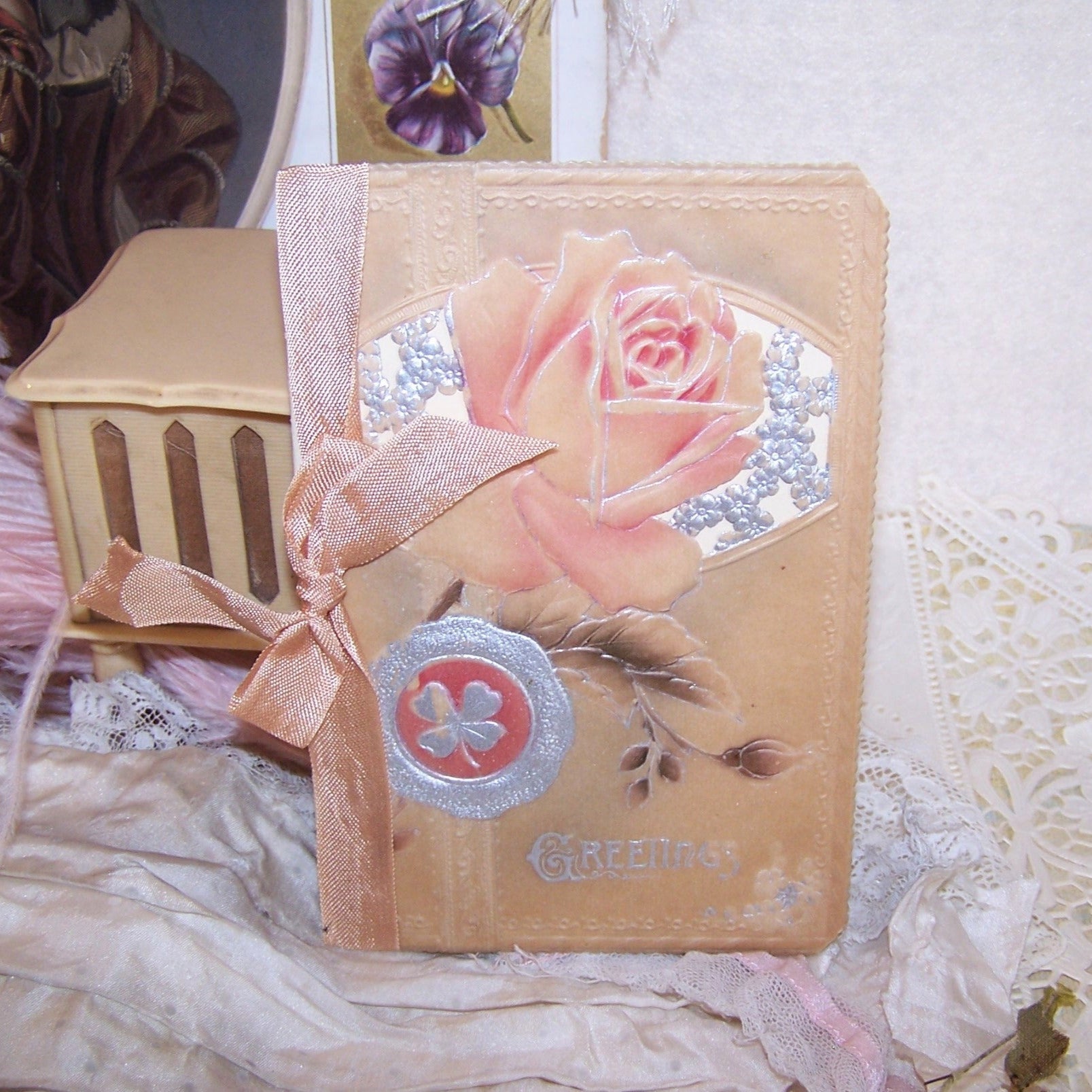 Christmas greeting card with an embossed celluloid cover of roses and 4 leaf clovers; the front sentiment is GREETINGS. Open the card to reveal a clean interior with a small Christmas poem. 