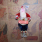 Vintage-style Santa Claus ornament with 'GREETINGS' sign on a decorative background