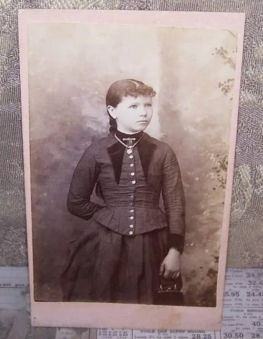 Taken during the late 1890s or so, here's an Antique&nbsp;Victorian cabinet card depicting the portrait of a young girl. She stands with one arm holding a cloth purse and the other tucked behind her back. She wears 2 pieces of gold filled jewelry - a bar pin and a necklace.&nbsp; Size is 2-1/2" x 4-1/8" approx.&nbsp; Condition is very nice with maybe just a tiny mark or two (and some dust speckles).