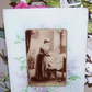 Antique sepia print under glass depicting a mother and child in the nursery. Border image of  hyacinths that may be the artwork of Catherine Klein (C. Klein).