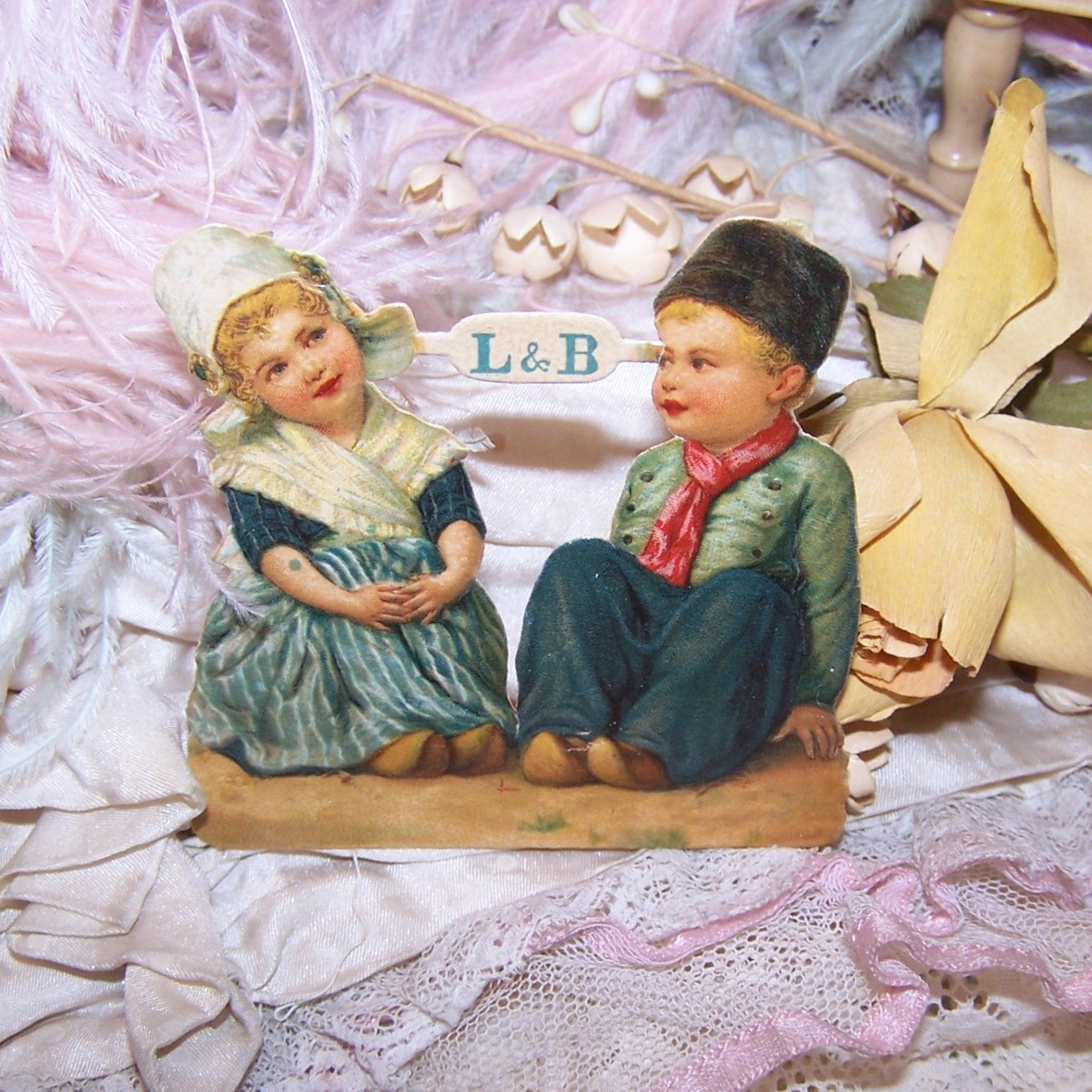 Antique Victorian die cut printed by L&B, the design number is 3847 and the image is of a Dutch Boy & Girl sitting on the ground. 2-1/2" wide x 2-11/16".