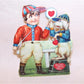 Here's an Art Deco mechanical high gloss Valentines Day card. The image is of a young boy dressed as a horse racing jockey holding up a heart sign to his dog (also dressed in horse racing garb). The hand of the boy and the paw of the dog move back and forth meeting in a HIGH FIVE sign. 