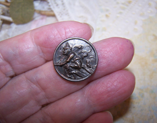Art Deco metal Halloween panel that I believe was once a pinback. 3/4" round with good strike of a witch riding her broom; at the end of the broom is her pet cat. 