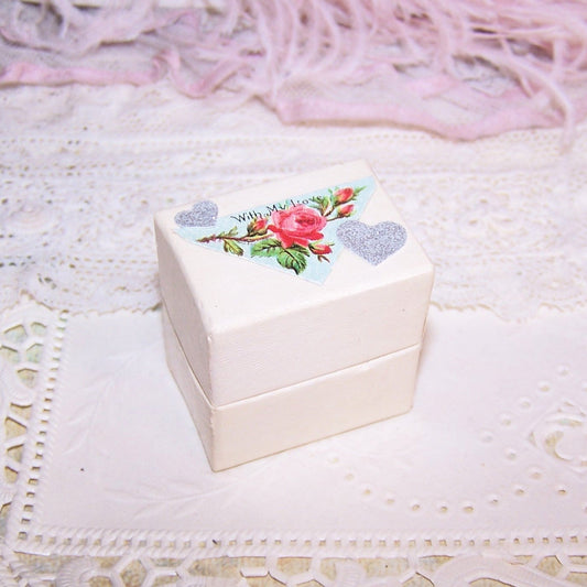 Cream paper ring box with slotted insert on the inside and Antique Victorian die cut reading WITH MY LOVE to the top.  1-1/2" high; base is 1-7/16" x 1-1/16"