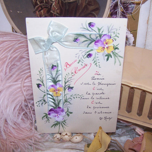 From France, an Antique handpainted postcard, unused, for a Bonne Annee. With an applied ribbon bow, the side lengths are painted with light purple and yellow pansies.