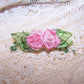 Antique French ribbonwork - a pair of pink ribbon flowers with green French striped ombre ribbon leaves. Further decoration of sugar pips.  1-3/4" x 9/16".