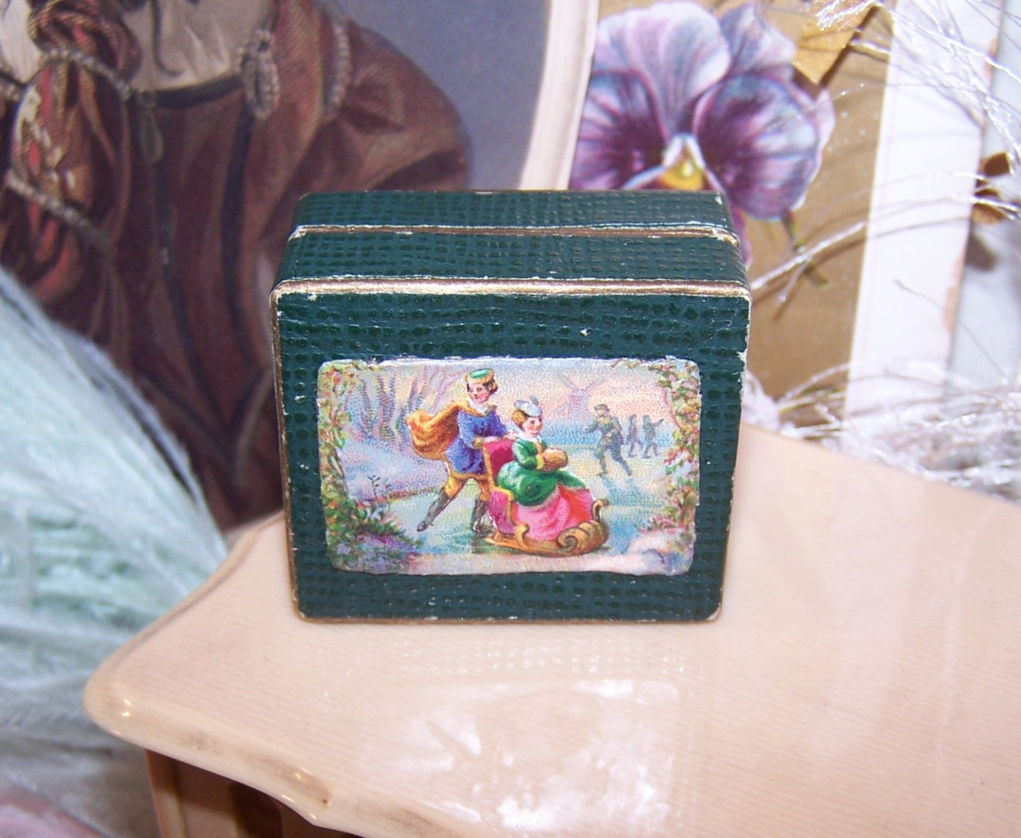 Antique Italian mini jewelry box. Dk green hinged lid has Victorian die cut of a gent ice skating, pushing a young lady in a small chair. Shabby Chic look