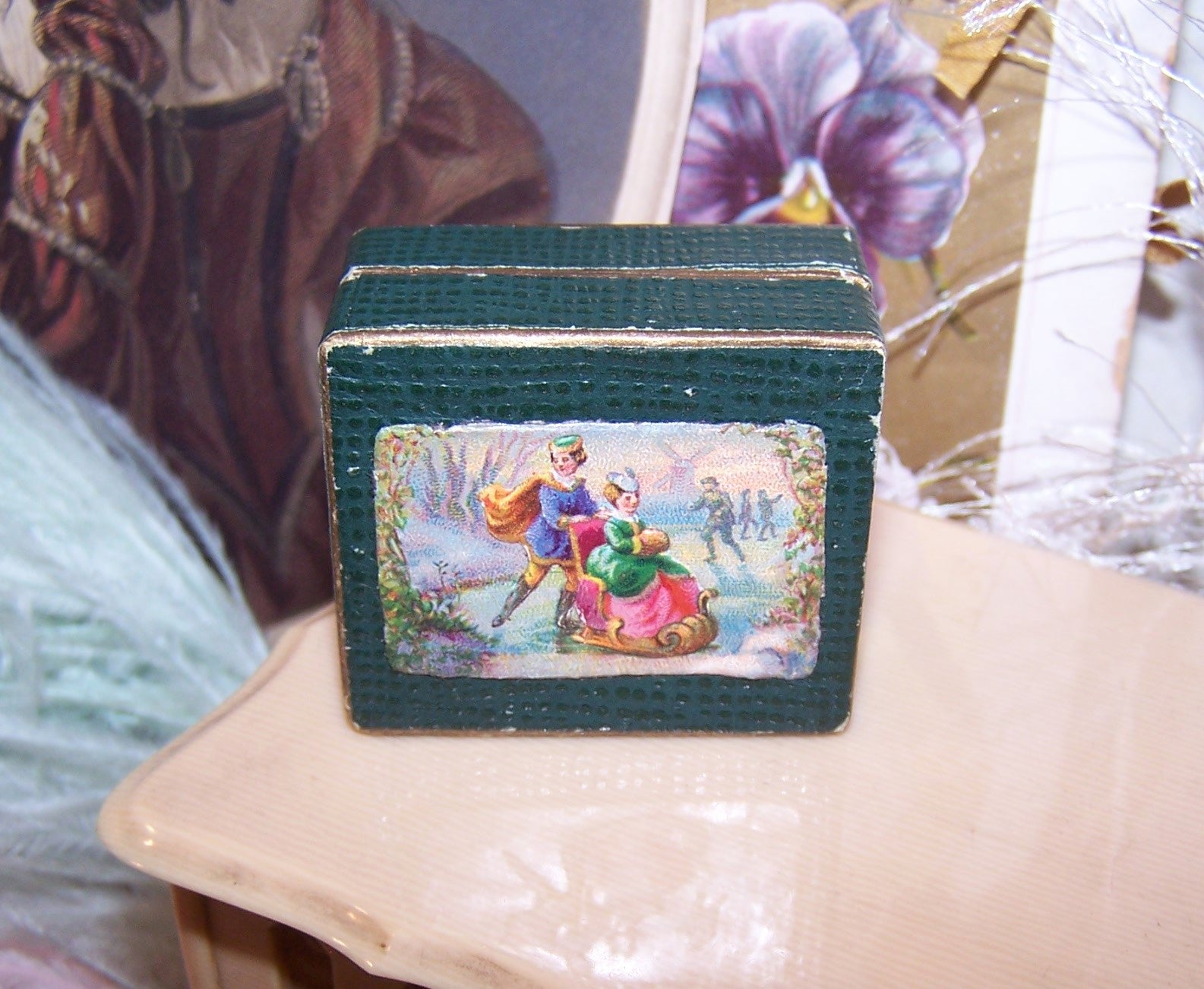 Antique Italian mini jewelry box. Dk green hinged lid has Victorian die cut of a gent ice skating, pushing a young lady in a small chair. Shabby Chic look