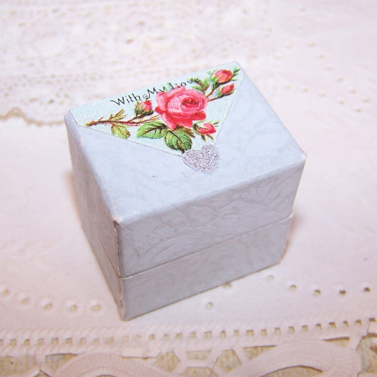 Light blue paper ring box with slotted insert on the inside and Antique Victorian die cut reading WITH MY LOVE to the top. 1-1/4" x 15/16" x 1-3/16" high. 