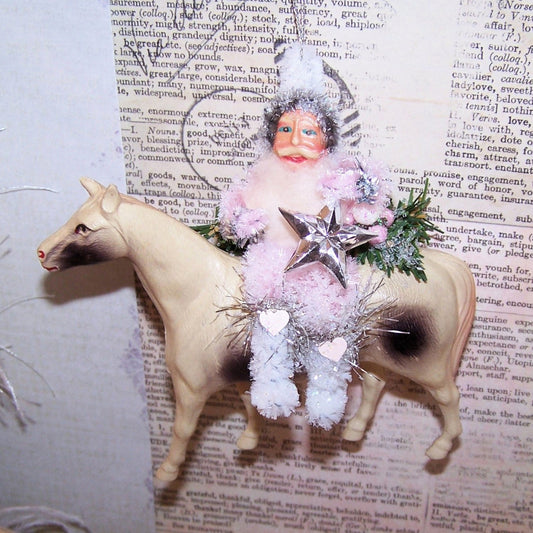 Handcrafted chenille & 1950s Japan paper face Santa Claus sitting on an Art Deco celluloid horse. He holds a silver star & sits amidst greenery.  5" x 4-3/4"