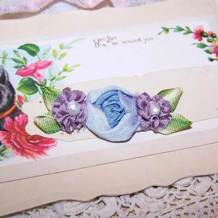 French Revival ribbonwork spray of 3 florals - a blue silk cabbage rose shouldered by a pair of mauve silk florettes, the centers set with freshwater pearls. 