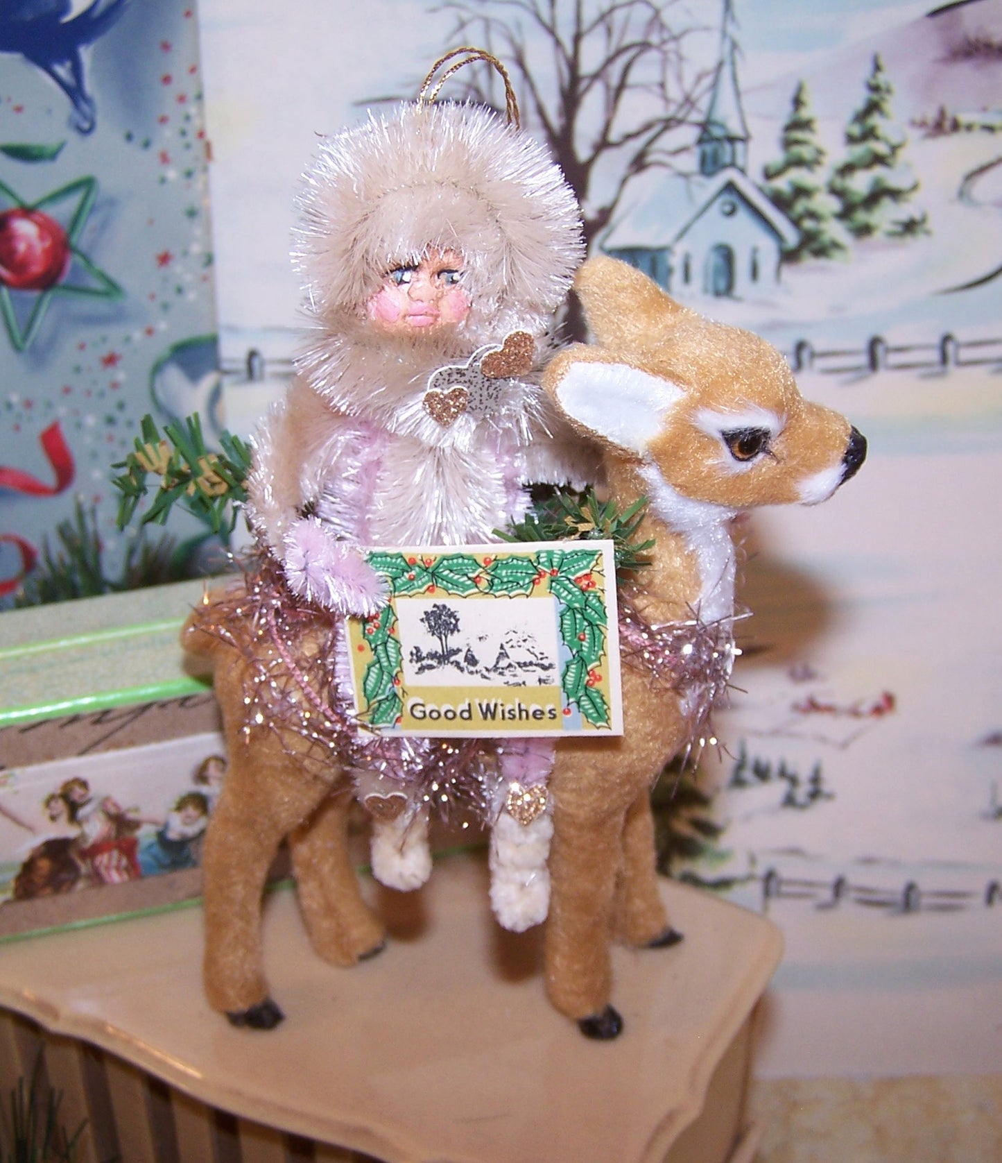 Original mixed media holiday ornament. My pink chenille girl sits on a brown fawn and holds a sign that reads GOOD WISHES.  5-1/2" x 3-1/2"
