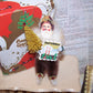For the Cabin! Brown tone chenille holiday ornament of Santa Claus.  Retro inspired, he carries a bottle brush Christmas tree and BEST WISHES signage. 3.5" High