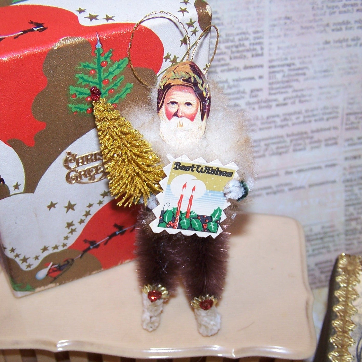 For the Cabin! Brown tone chenille holiday ornament of Santa Claus.  Retro inspired, he carries a bottle brush Christmas tree and BEST WISHES signage. 3.5" High