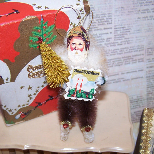 For the Cabin! Brown tone chenille holiday ornament of Santa Claus.  Retro inspired, he carries a bottle brush Christmas tree and BEST WISHES signage. 3.5" High