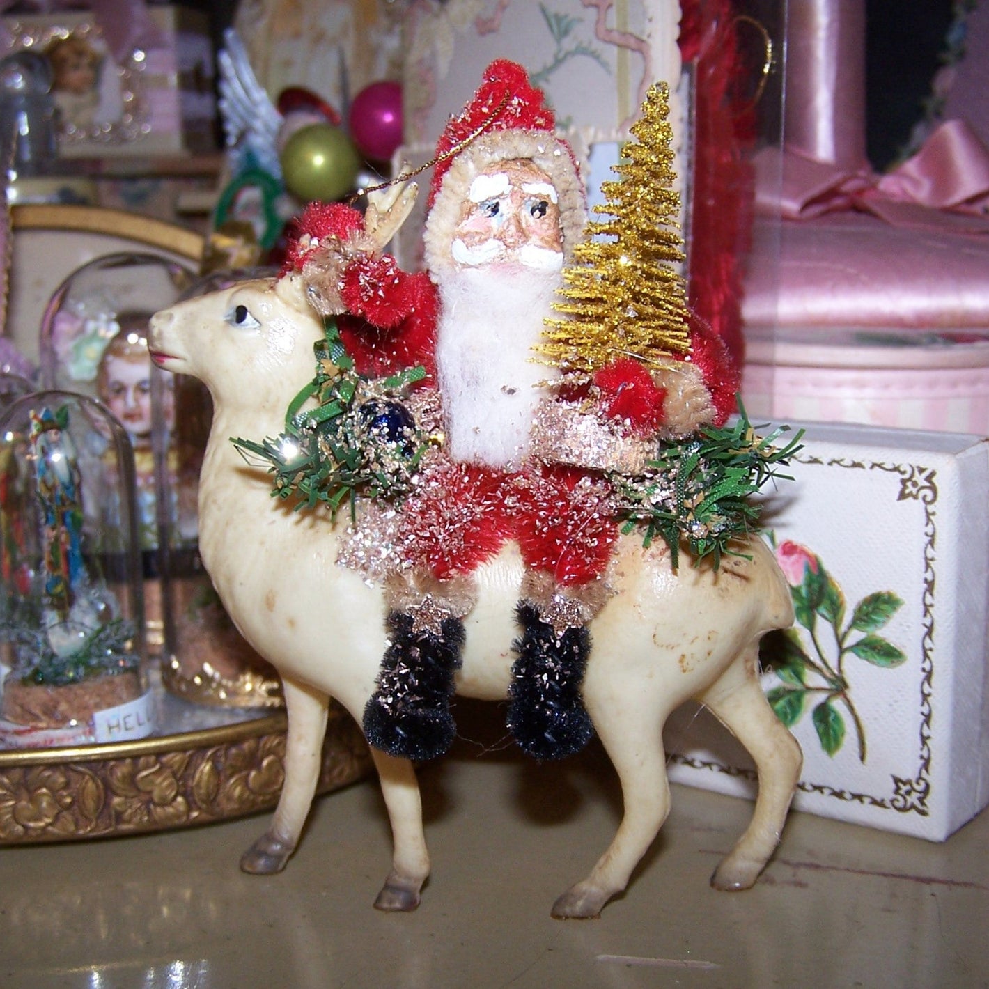 Handcrafted chenille & clay face Santa Claus sitting on one of his reindeer. He holds a gold Christmas tree, & sits amidst greenery. 4-1/2" high x 3-3/4" high. 