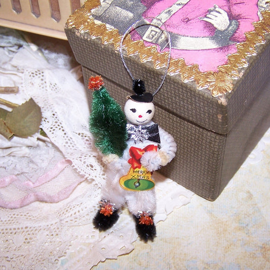 Handcrafted mixed media ornament of Frosty the Snowman.  In a retro inspired design, Frosty  carries a chenille Christmas tree and Merry Xmas paper bell. 