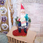 Handcrafted One of a Kind chenille & clay face Santa Claus sitting on a sequined boot ornament/mantel decoration. He holds a sign reading GREETINGS. 5.5" x 2.5"