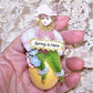 Handmade chenille ornament designed in a Victorian Revival manner.  A little girl sits on a sparkly Easter Egg and holds a sign that reads SPRING IS HERE. 