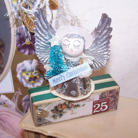 Upcycled 1960s Made in Japan foil, Dresden paper and glitter angel ornament.  Pale pink and silver coloring.  Stands 2-3/4" high; width is 2-1/4". 